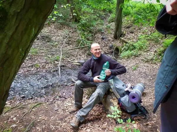 Mann sitzt auf einem Baumstumpf und hält eine Wasserflasche in der Hand