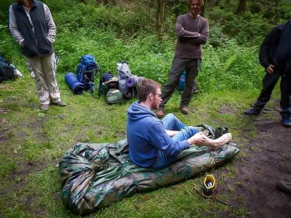 Mann sitzt auf einer improvisierten Unterlage aus Folie im Wald