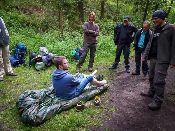 Mann sitzt auf einer Tarp-Notunterkunft, umgeben von mehreren Personen und Rucksäcken