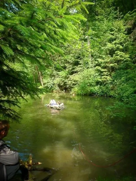Mann steht am Ufer eines klaren Gewässers, umgeben von dichtem Grün