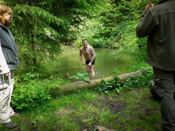 Mann steht im Wasser eines kleinen Gewässers, umgeben von Bäumen und Pflanzen