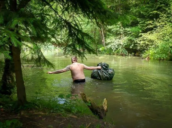 Mann watet mit einem Müllsack durch einen klaren Fluss