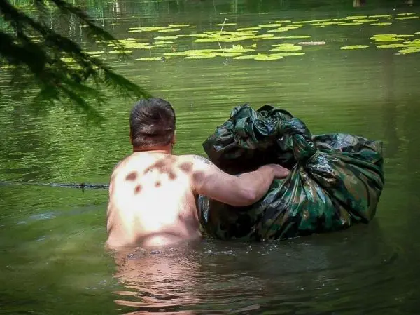 Mann zieht einen großen, camouflagierten Sack durch das Wasser