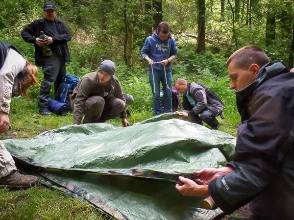Mehrere Personen bauen eine Tarp-Notunterkunft im Wald auf