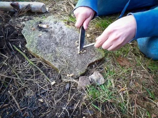Messer schabt Holzspäne von einem Stein auf dem Boden