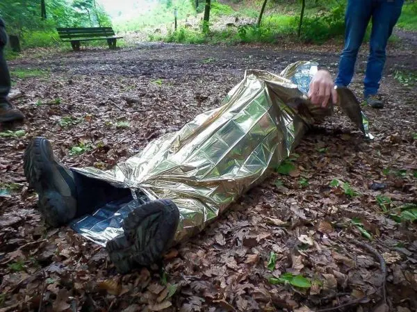 Person in Rettungsdecke liegt auf dem Boden, während eine andere Person hilft
