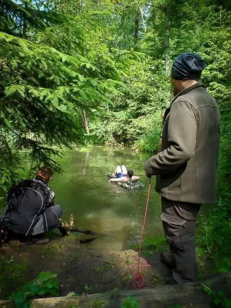 Person mit Seil beobachtet andere Person im Wasser, während eine dritte Person am Ufer sitzt