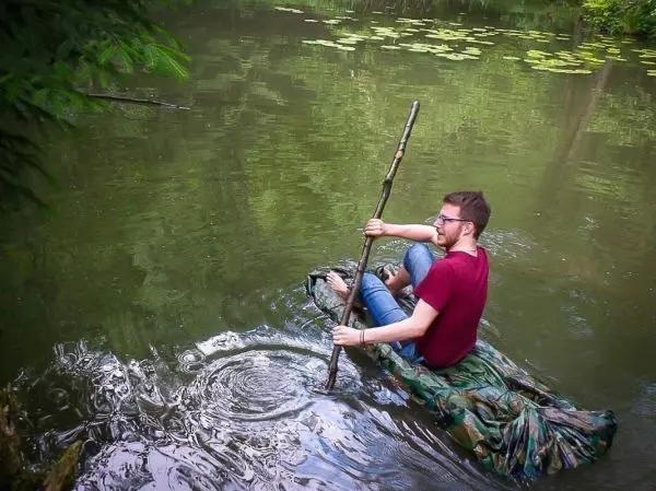 Person paddelt auf einem selbstgebauten Floß im Wasser