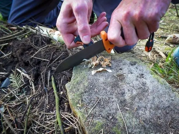 Person schneidet Holzstücke mit einem Messer auf einem Stein