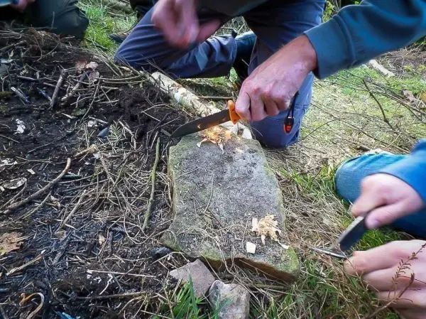 Person schneidet mit einem Messer Holzspäne auf einem Stein