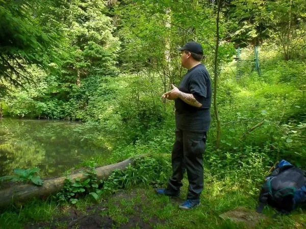 Person steht am Ufer eines kleinen Teichs im Wald