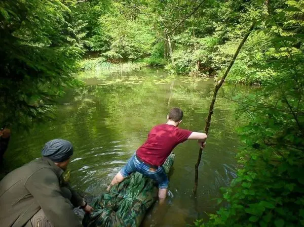 Person steht auf einer improvisierten Plattform im Wasser und hält einen Stock