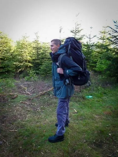 Person trägt einen großen Rucksack und steht in einem Waldgebiet