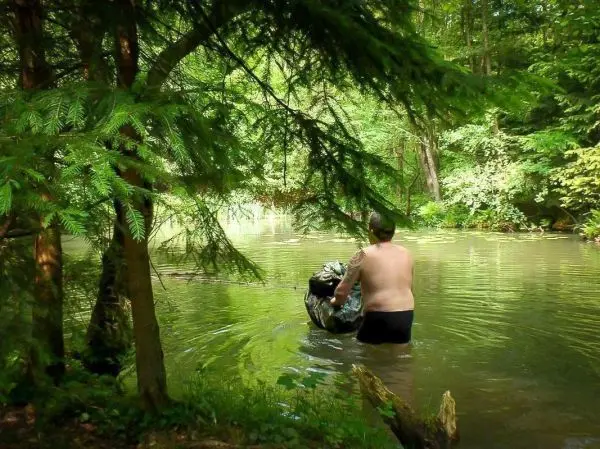 Person trägt einen Rucksack im Wasser eines Waldbachs