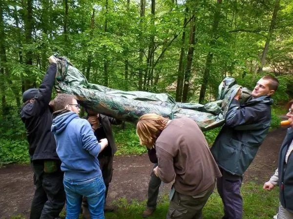 Sechs Personen heben eine Tarp-Notunterkunft im Wald an