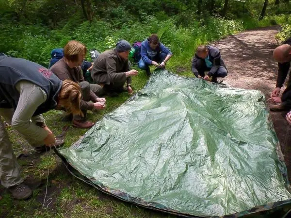 Sechs Personen spannen eine Tarp-Notunterkunft auf dem Boden