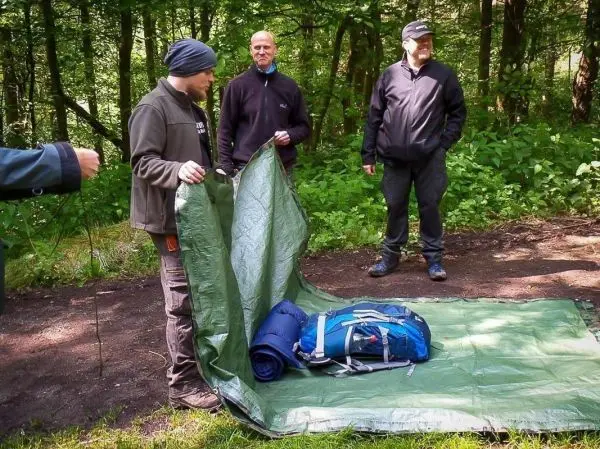 Tarp-Notunterkunft wird auf dem Boden ausgebreitet, Rucksack und Schlafsack liegen darauf