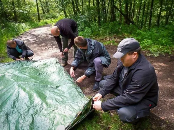 Tarp-Notunterkunft wird von mehreren Personen auf dem Boden befestigt