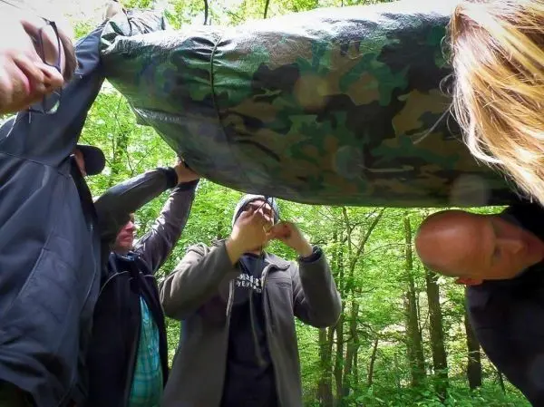 Tarp-Notunterkunft wird von mehreren Personen aufgebaut und gesichert