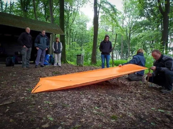 Tarp-Notunterkunft wird von zwei Personen mit Heringen befestigt