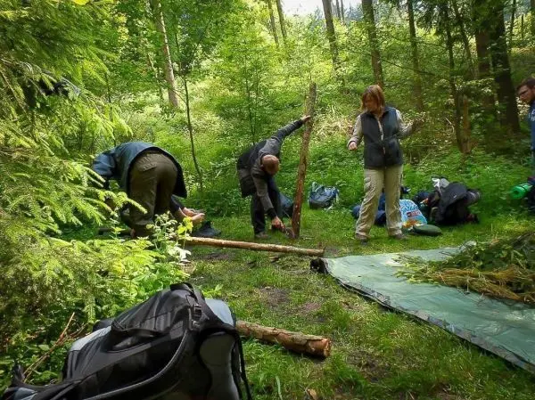 Teilnehmer bauen eine Tarp-Notunterkunft im Wald mit Holzstöcken