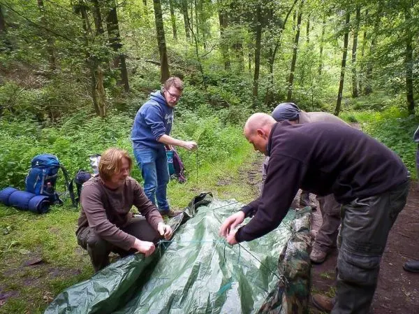 Vier Personen bauen eine Tarp-Notunterkunft im Wald auf