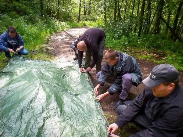 Vier Personen befestigen eine grüne Tarp-Notunterkunft auf dem Boden