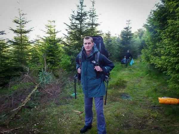 Wanderer mit Rucksack auf einem Waldweg zwischen Nadelbäumen