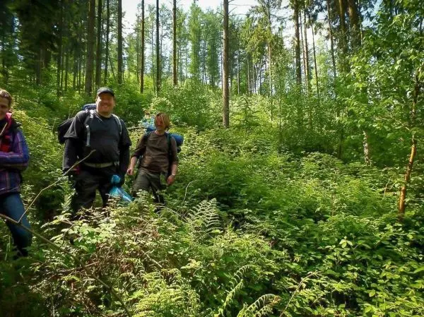 Wanderer mit Rucksäcken bewegen sich durch dichten Wald mit hohem Unterholz