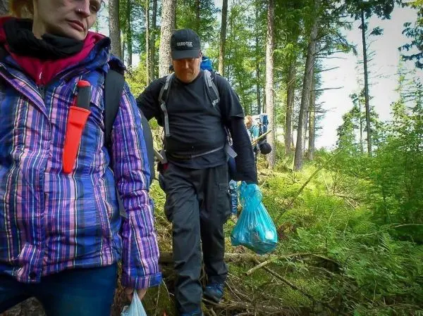 Wanderer tragen Müllsäcke auf einem Waldweg zwischen Bäumen