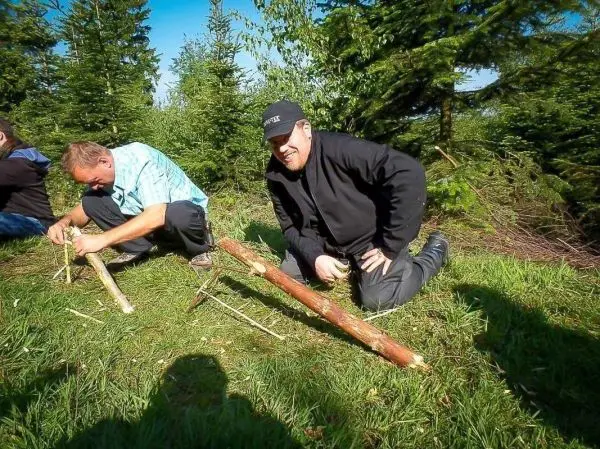 Zwei Personen arbeiten am Boden mit Holzstücken und Schnüren zur Konstruktion