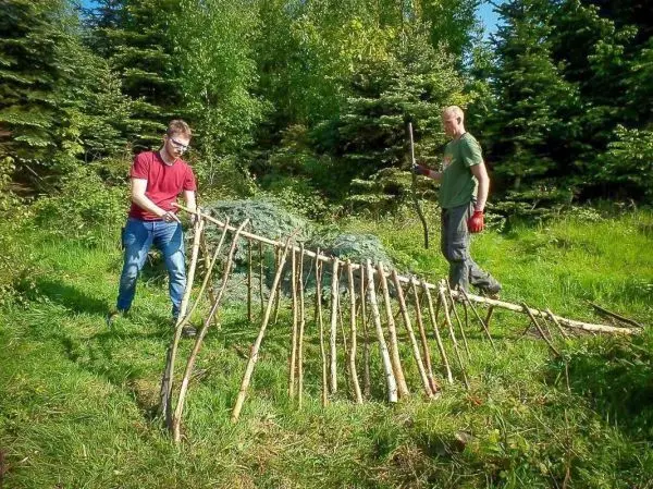 Zwei Personen bauen eine selbstgebaute Konstruktion aus Ästen im Wald