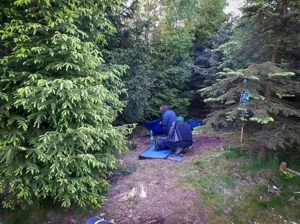 Zwei Personen bereiten eine Tarp-Notunterkunft im Wald vor
