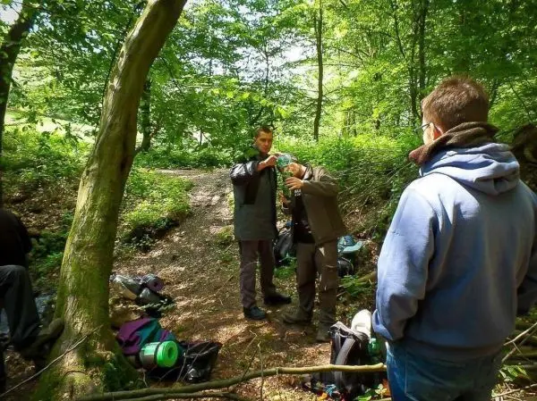 Zwei Personen füllen Wasser aus einer Flasche in einen Behälter im Wald