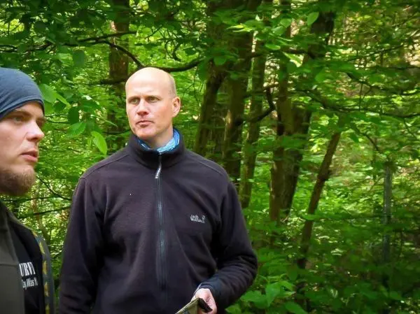 Zwei Personen stehen im Wald zwischen grünen Bäumen und diskutieren