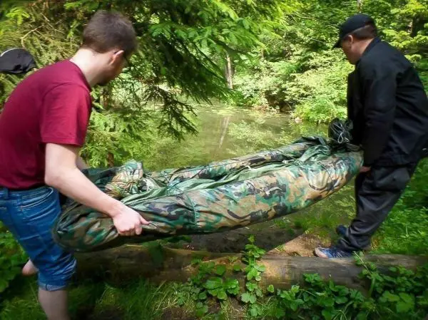 Zwei Personen tragen ein camouflagefarbenes Boot zum Wasser