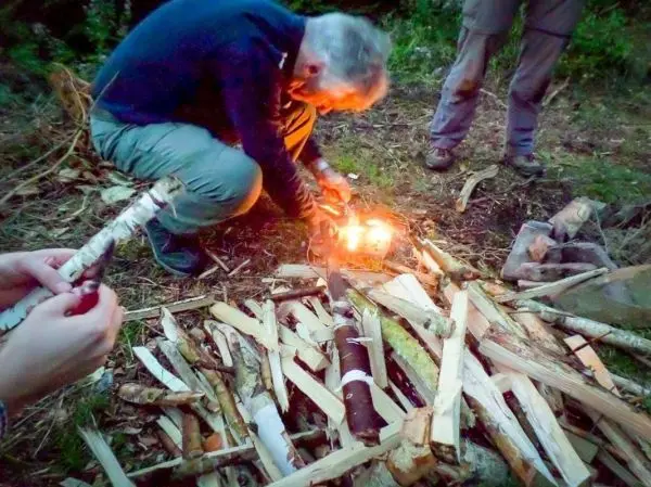 Feuerstahl erzeugt Funken auf Zunder zwischen Holzscheiten