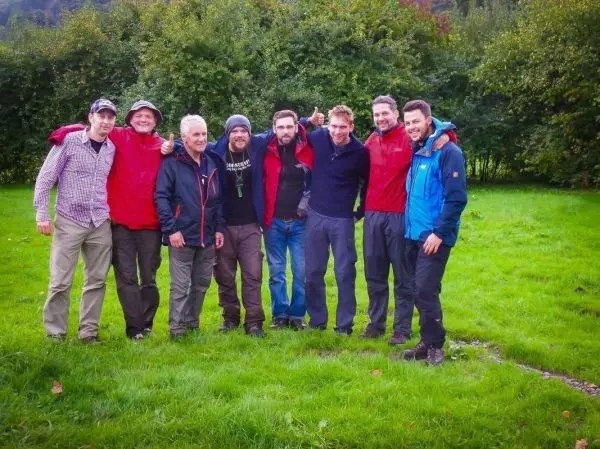 Gruppe von acht Personen steht lächelnd auf einer Wiese, umarmt sich