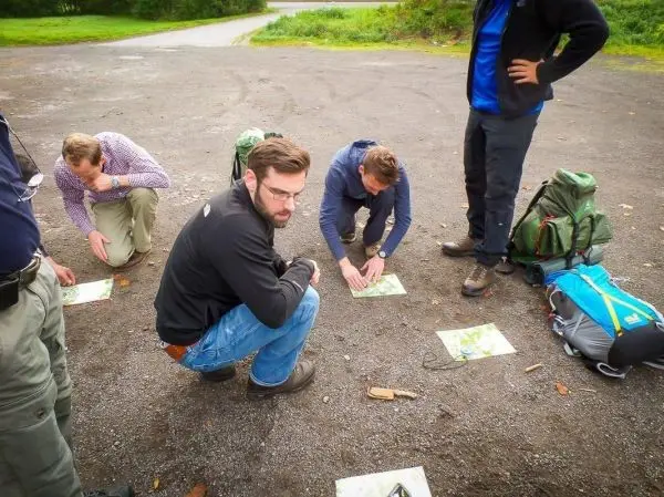 Gruppenteilnehmer studieren Karten auf dem Boden, Rucksäcke liegen daneben