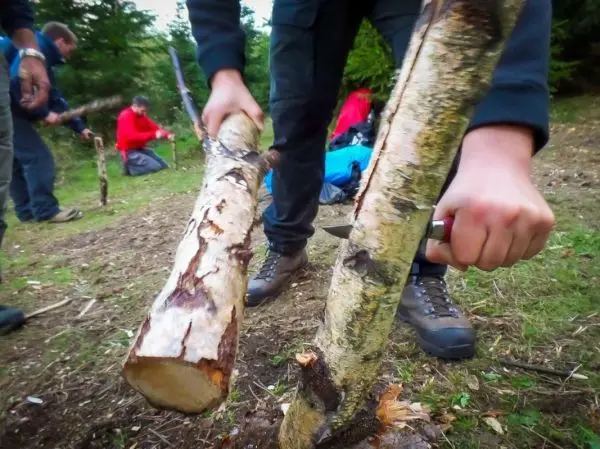 Holzstück wird mit einem Messer bearbeitet, während andere Teilnehmer im Hintergrund arbeiten