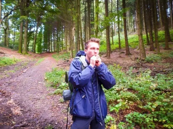 Junge bläst in eine Pfeife auf einem Waldweg zwischen Bäumen