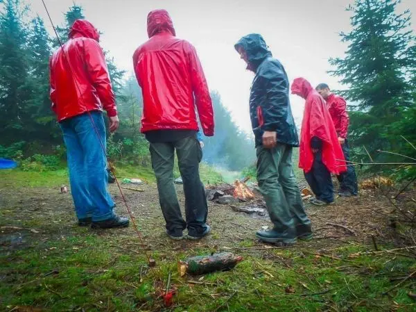 Kleine Flamme brennt im Hintergrund, während Personen in Regenjacken stehen