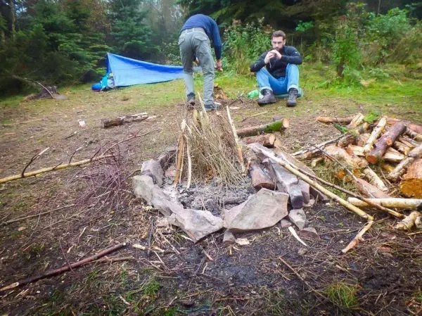Kleine Flamme in einer Feuerstelle aus Steinen, Holzstapel im Hintergrund