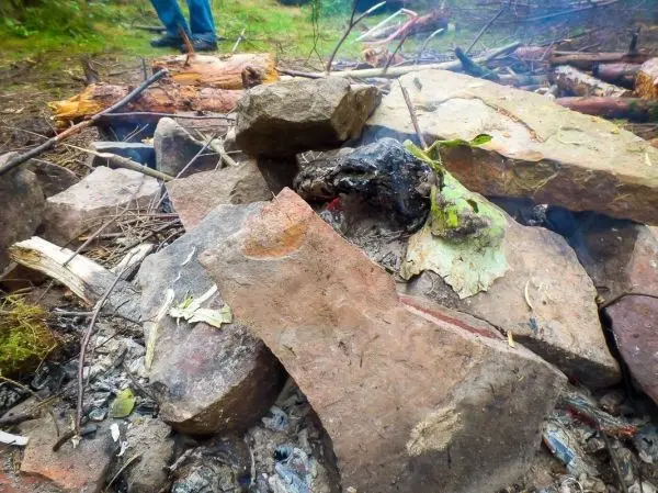Kleine Flamme und glühende Kohlen zwischen Steinen im Bodenfeuer