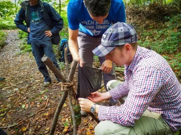 Mann bindet ein Tuch an eine selbstgebaute Konstruktion aus Ästen