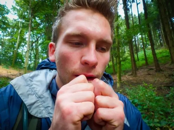 Mann bläst in seine Hände zur Wärme im Wald