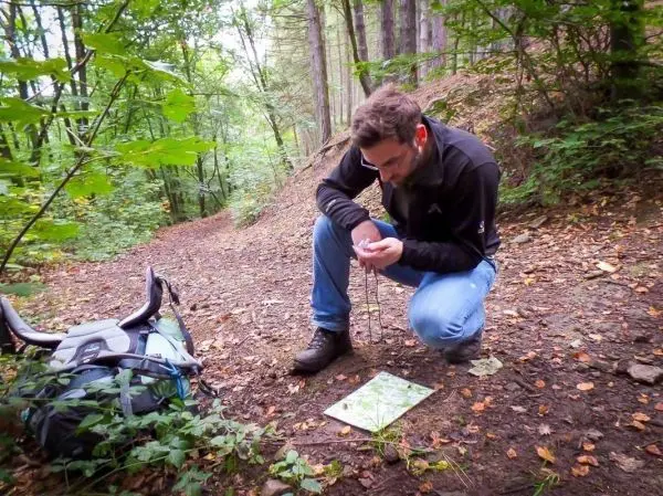 Mann kniet auf dem Waldboden und betrachtet eine Karte