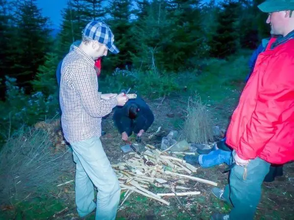 Messer schneidet Holzstücke für ein Feuer, während andere beobachten