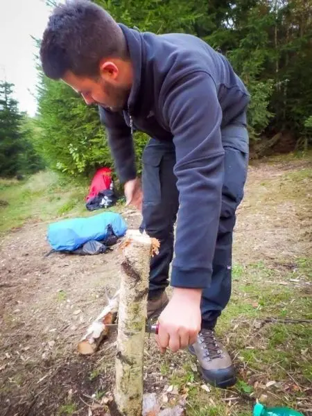Person bearbeitet einen Baumstamm mit einem Messer beim Überlebenstraining