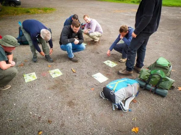 Sechs Personen analysieren Karten auf dem Boden, Rucksäcke liegen daneben